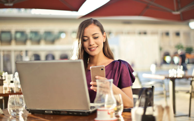 meisje op zoek naar telefoon tijdens het werken buiten op haar laptop