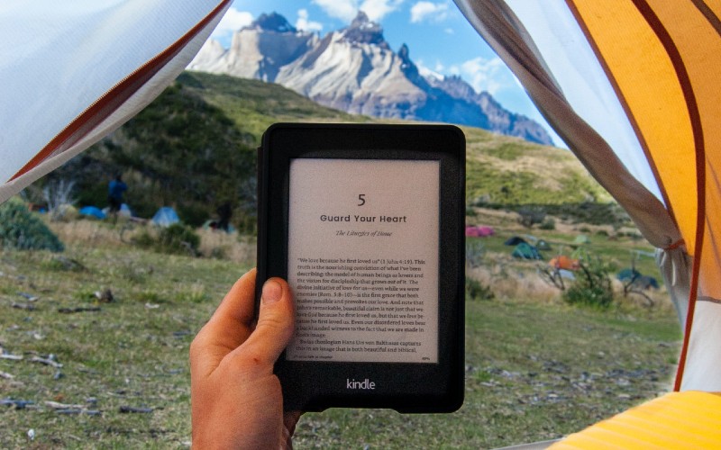 Someone reading on an Amazon Kindle in a tent while traveling through the mountains