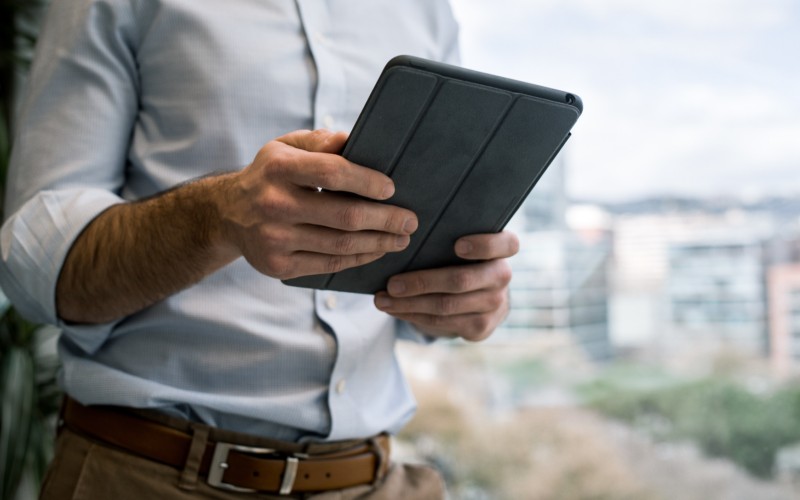 A professional looking man holding a tablet in a grey cover.