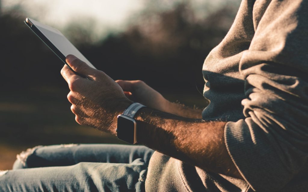 Man wearing an Apple watch and reading from a tablet