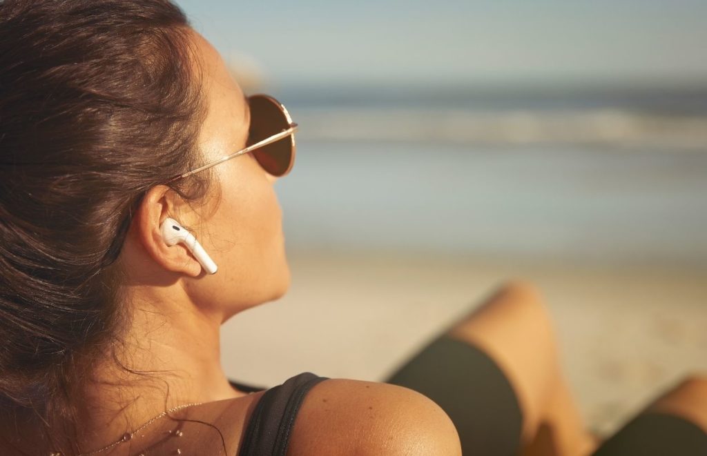 A lady using AirPods while lying on the beach