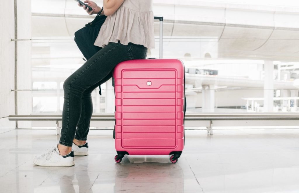 A lady sat on a pink hard-shelled suitcase, a hardshell is highly advised when packing wine in checked luggage.