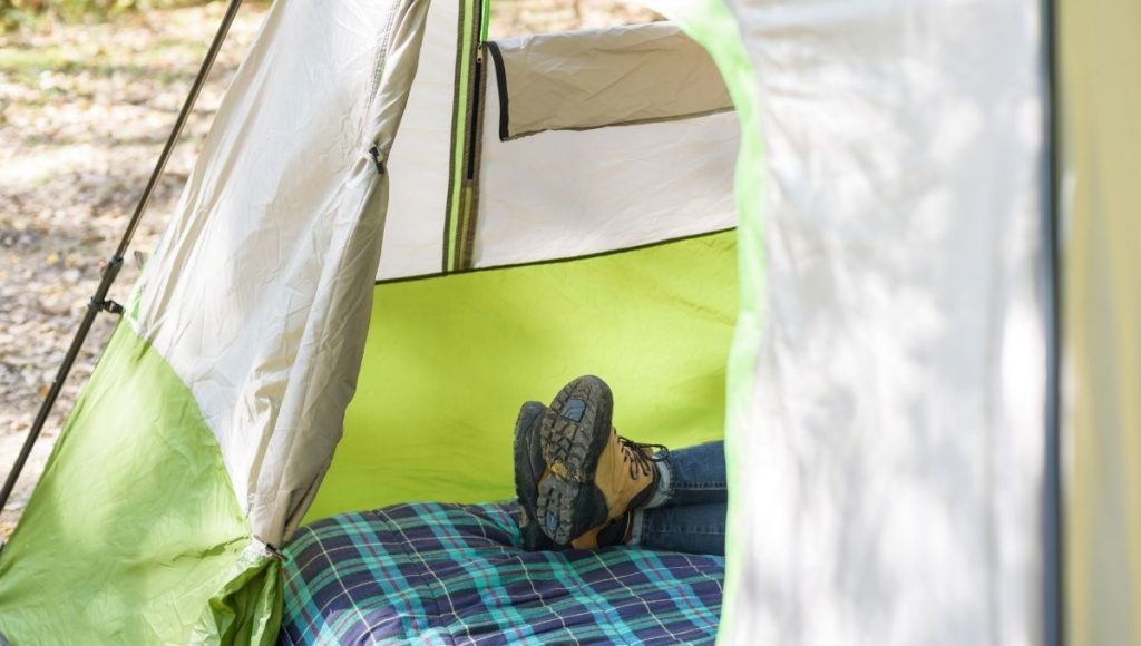 A man lying on a camping cot in a tent with muddy shoes on