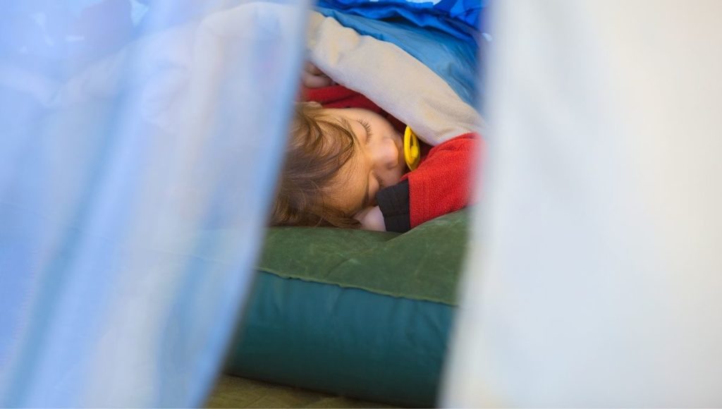 A child in a tent sleeping on an air mattress