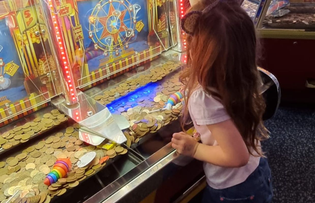 A young girl playing with a penny push machine in the Looe arcade