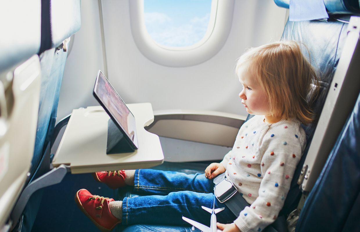 A toddler watching a tablet while in an aeroplane seat.