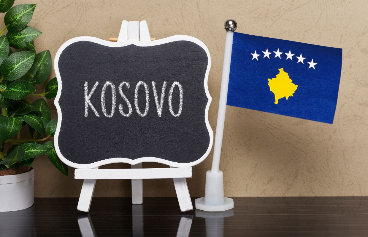 A Kosovo flag next to a small chalkboard with Kosovo written on it.