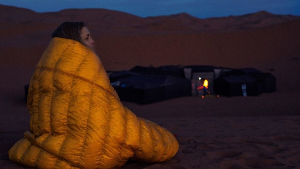 A girl wrapped in a sleeping bag in the cold dessert at night