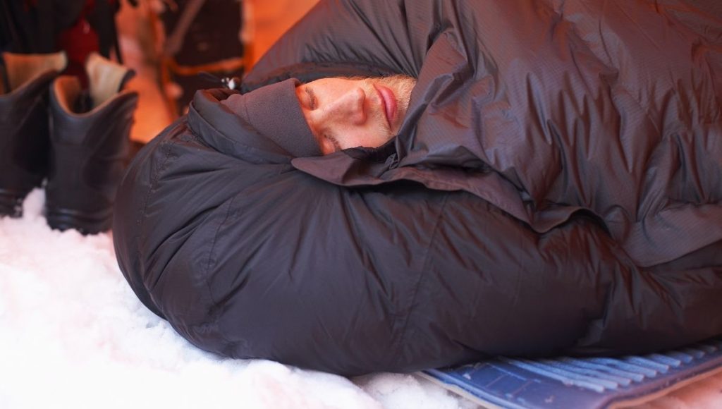 A man wrapped up in a sleeping bag with snow on the ground