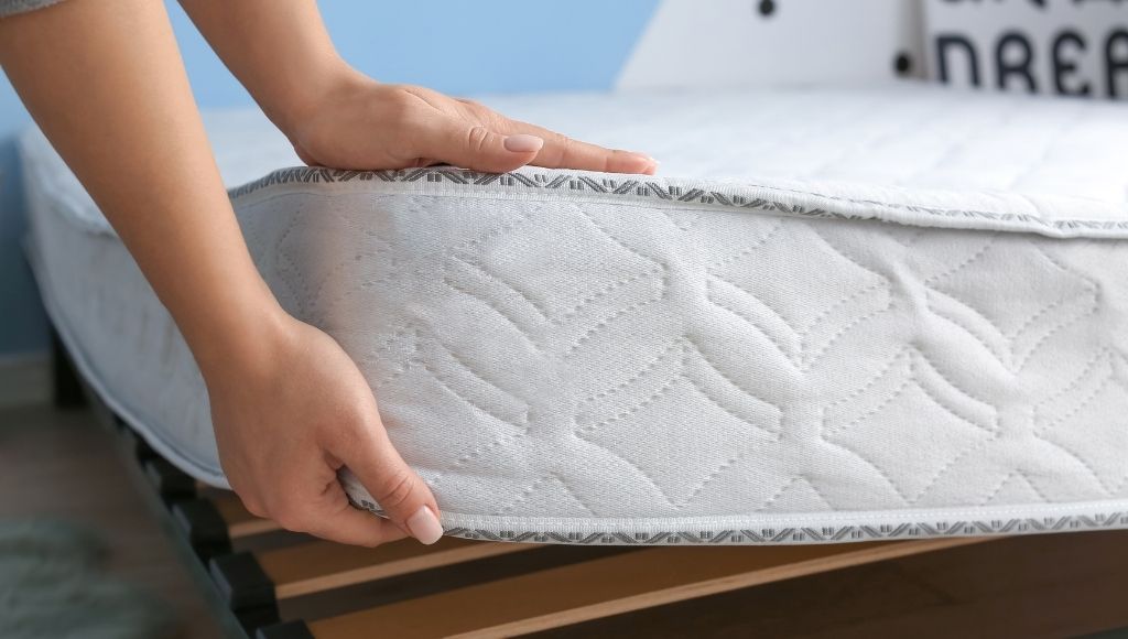A woman is holding a corner of a foam mattress with her hand