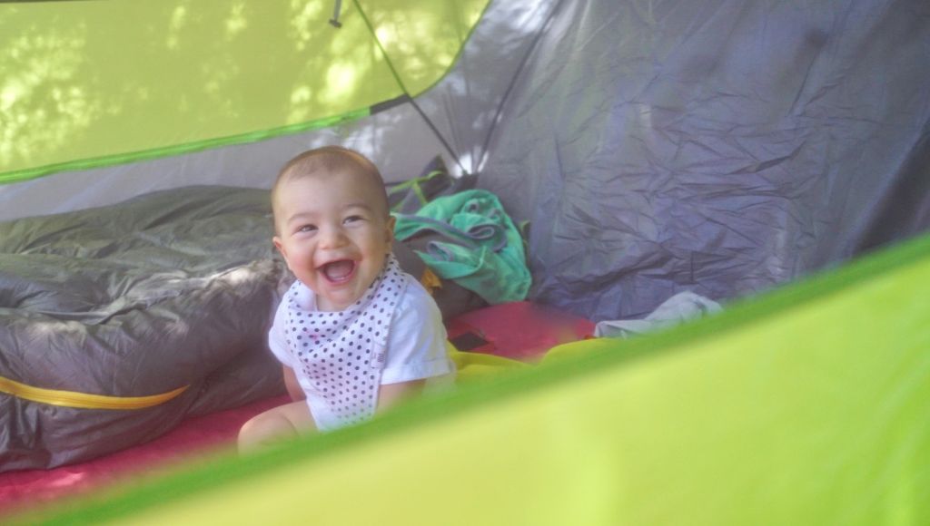 A baby sits inside a tent and laughs