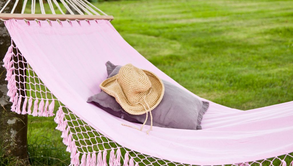 There is a pillow and a hat on the pink colored hammock