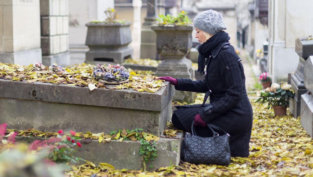 A woman mourning with her hand on headstone remembering dead relatives in pere lachaise cemetery in paris