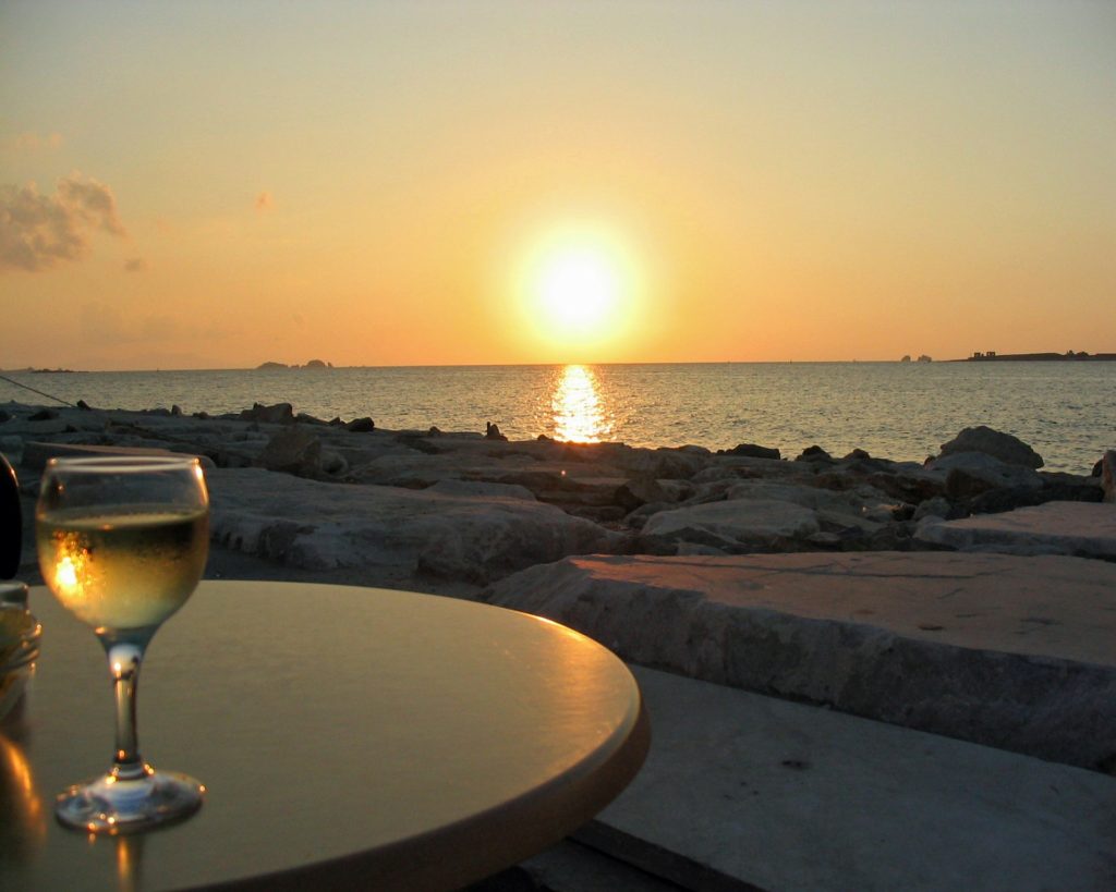 A glass of wine on a table close to the beach with the sunset 