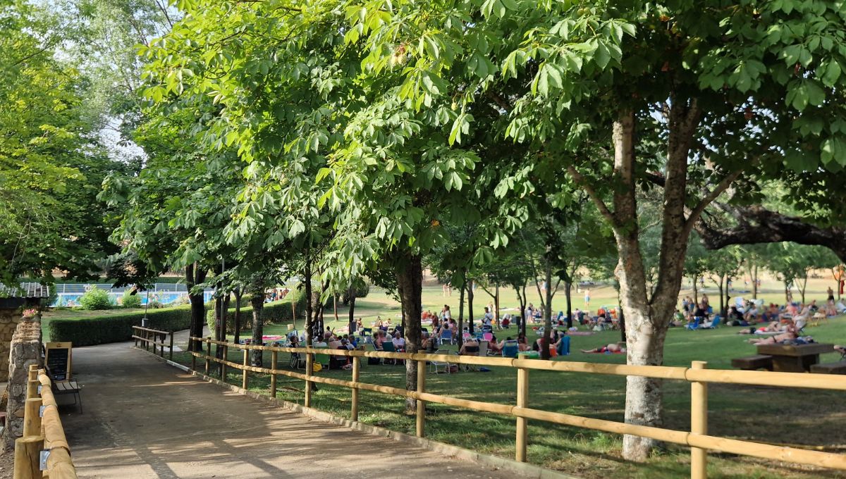 The fenced path that leads to the pools at Piscina Municipal Serradilla del Arroyo with people gathering in the shade of the trees