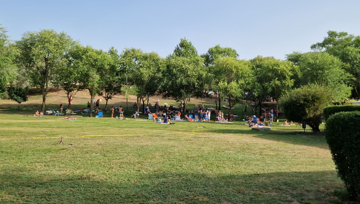 The wide open space at Piscina Municipal Serradilla del Arroyo with people relaxing on the grassy spots under the shade of the many trees