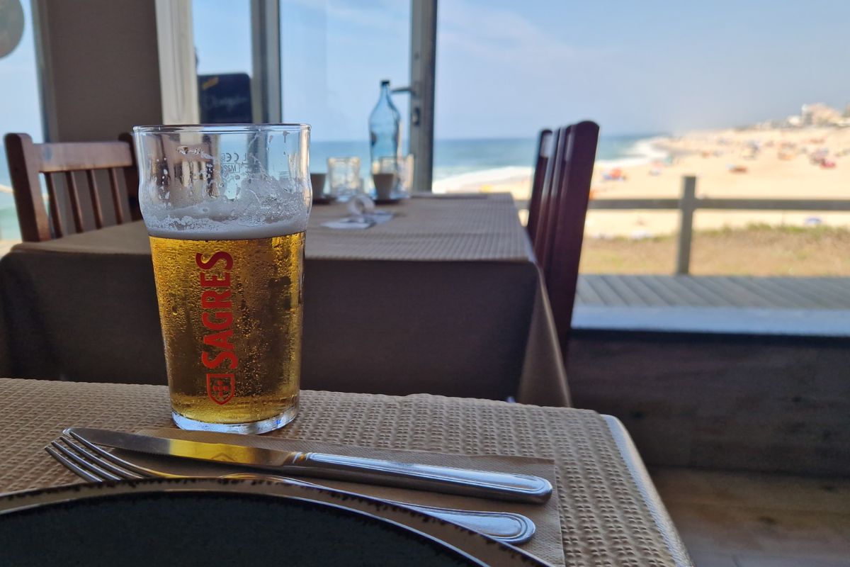 My beer in the foreground on my table with a window view across to Praia do Pedrogao beach.